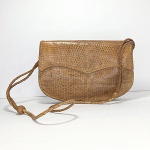 May include: A tan leather purse with a braided strap. The purse has a textured, snakeskin-like pattern.