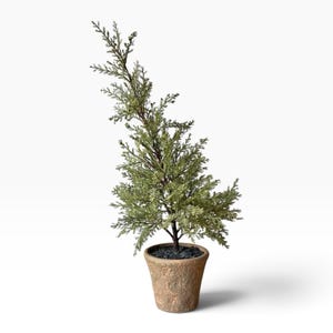 May include: A small artificial evergreen tree with needle-like foliage in shades of muted green and brown. The tree is planted in a textured, light brown tapered pot filled with dark gray decorative stones at the base of the trunk.