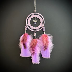 May include: A purple dreamcatcher with a silver chain and a small silver butterfly charm. The dreamcatcher has three purple feathers with pink and white accents.