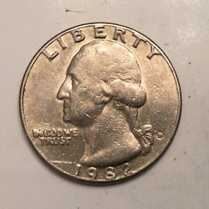 Puede incluir: Una moneda de un cuarto de dólar estadounidense de plata con el año 1982 inscrito en la parte inferior. La moneda presenta un perfil de Lady Liberty con las palabras "LIBERTY" arriba y "IN GOD WE TRUST" abajo.