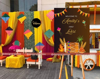 May include: A brown welcome sign on a wooden easel featuring the text Welcome to Amitoj's First Lohri, decorated with illustrations of a dhol drum, a bonfire, wheat stalks, and colourful kites, set against a backdrop of draped fabric.