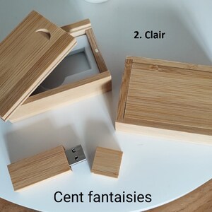 Op de afbeelding: Twee houten dozen met deksels, een open en een gesloten, en een houten USB-stick met een metalen connector. De dozen zijn gemaakt van lichtbruin hout met een natuurlijke nerf. De USB-stick is ook gemaakt van lichtbruin hout. De tekst "Cent fantaisies" is afgedrukt op het witte oppervlak onder de items.
