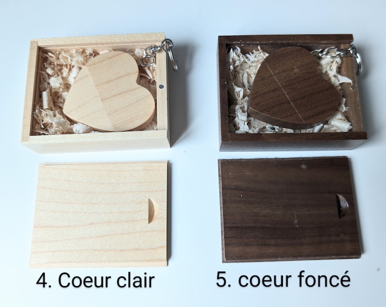 Op de afbeelding: Twee houten hartvormige sleutelhangers in dozen. De sleutelhanger links is van licht hout en de sleutelhanger rechts is van donker hout. Beide sleutelhangers zitten in hun eigen dozen met houtsnippers.