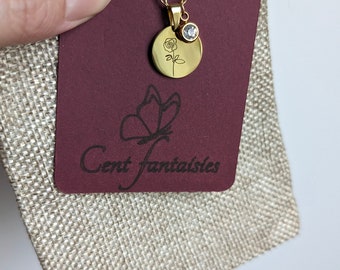Op de afbeelding: Een gouden ketting met een klein rond hangertje met een delicaat rozenmotief en een enkele heldere strasssteen. De ketting wordt gepresenteerd op een bordeauxrode kaart met een vlinderlogo en de tekst "Cent Fantaisies".