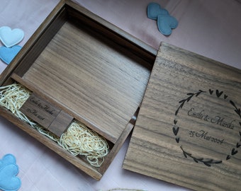 Könnte beinhalten: Eine Holzkiste mit einem Scharnierdeckel, graviert mit dem Text "Emilie & Marika 25 Mai 2024" und einem floralen Design. Die Kiste ist geöffnet und zeigt eine kleine Holz-USB-Stick mit dem Text "Emilie & Marika 25 Mai 2024" und einer Schicht aus zerkleinertem Holz.