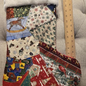 May include: A patchwork Christmas stocking with a white faux fur cuff. The stocking is made of various fabric patterns, including rocking horses, snowflakes, and gingerbread men. The stocking measures approximately 18 inches in length.