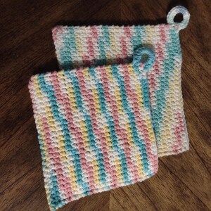 May include: Two crocheted pot holders in a striped pattern of pink, yellow, blue, and white. The pot holders have a loop handle.