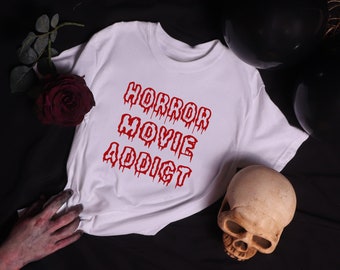 May include: White t-shirt with the text "HORROR MOVIE ADDICT" in red dripping letters. The shirt is on a black background with a skull and a rose.