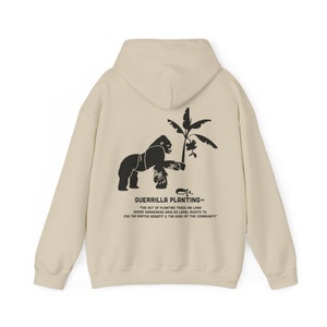 May include: A beige hoodie featuring a black gorilla graphic holding a palm tree. The text "GUERRILLA PLANTING - "THE ACT OF PLANTING TREES ON LAND WHERE GARDENERS HAVE NO LEGAL RIGHTS TO. FOR THE EARTHS BENEFIT & THE GOOD OF THE COMMUNITY" is printed on the back.
