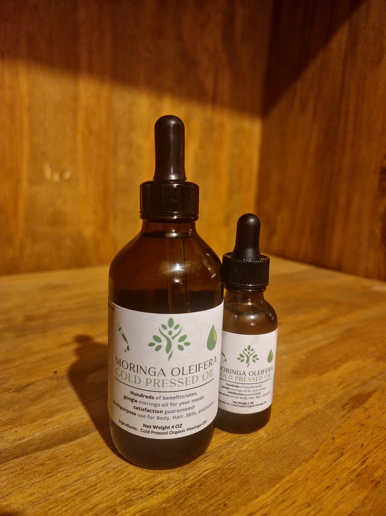 May include: Two glass bottles of Moringa Oleifera Cold Pressed Oil. The larger bottle is 4 oz and the smaller bottle is 1 oz. Both bottles have a dropper top and are labeled with the product name and ingredients.