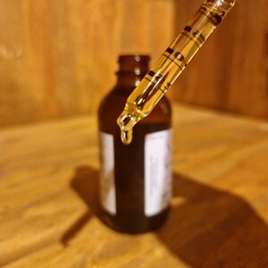 May include: A glass dropper with a clear liquid inside, dripping into a dark brown glass bottle with a label.