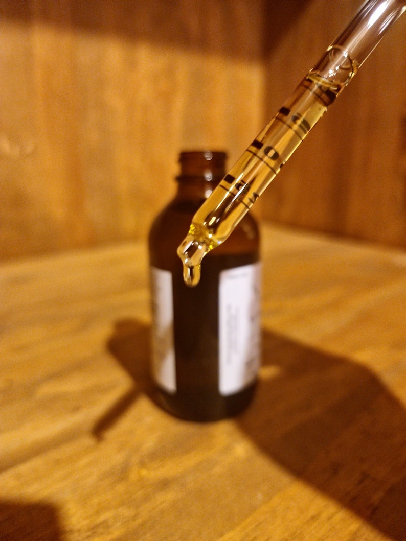 May include: A glass dropper with a clear liquid inside, dripping into a dark brown glass bottle with a label.