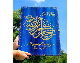May include: A blue canvas painting with gold calligraphy and the text "He put between you Love & Mercy" and "Maryam & Fayyaz August 6, 2021".