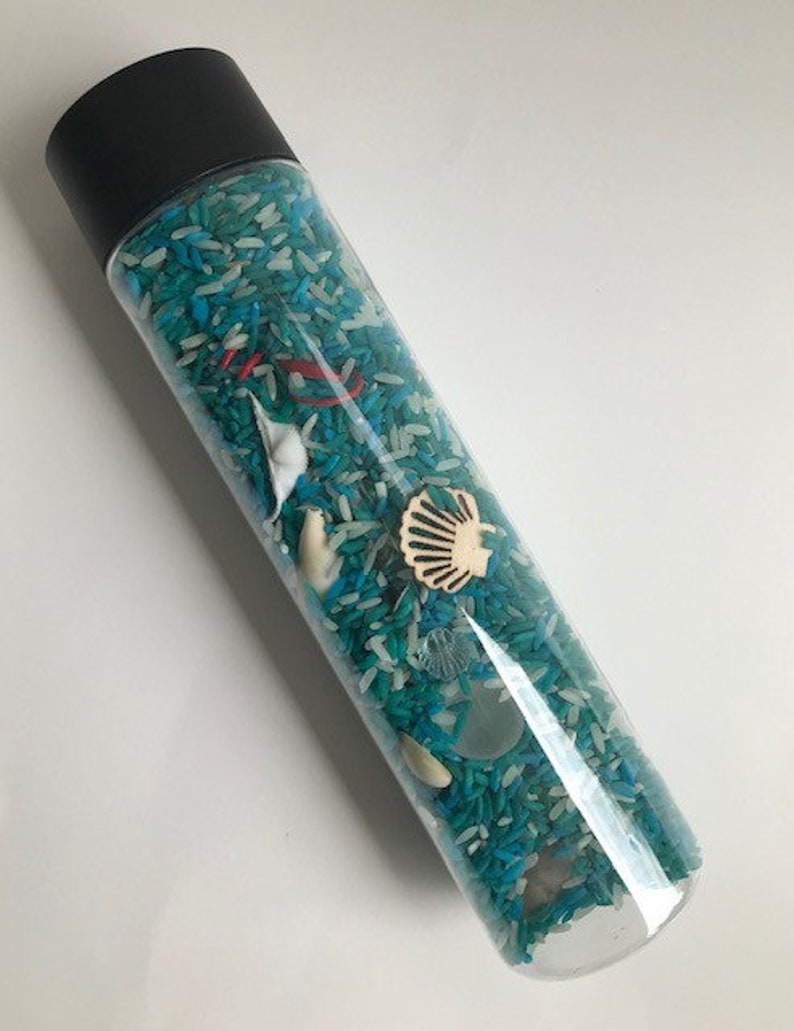 May include: A clear plastic bottle filled with white and blue rice, with various small sea-themed objects, including a seashell, a starfish, and a small piece of driftwood.