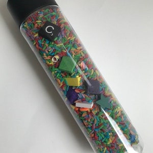 May include: A clear plastic bottle filled with colorful rice and small wooden shapes. The bottle has a black lid with the letter "C" and the number "3" on it.