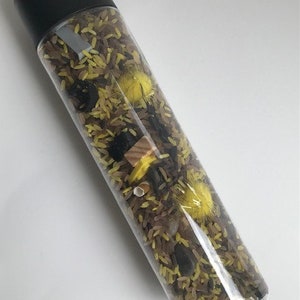 May include: A clear plastic bottle filled with brown and yellow rice, black beans, yellow pom-poms, and a small wooden block.