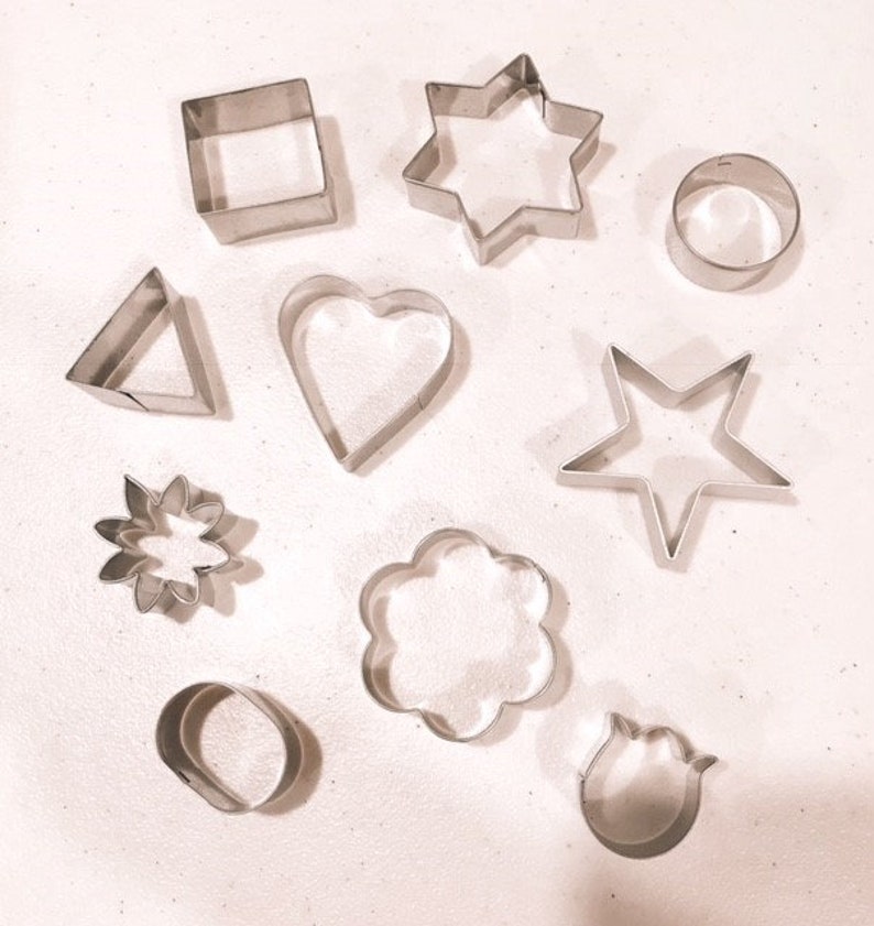 May include: A collection of stainless steel cookie cutters in various shapes, including a square, triangle, heart, star, flower, cloud, oval, circle, and tulip. These cutters are designed for baking and crafting.
