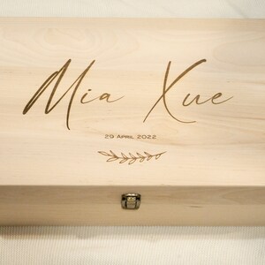 May include: A light wood keepsake box with a hinged lid and a brass latch. The box is engraved with the name "Mia Kue" and the date "29 April 2022" along with a small floral design.