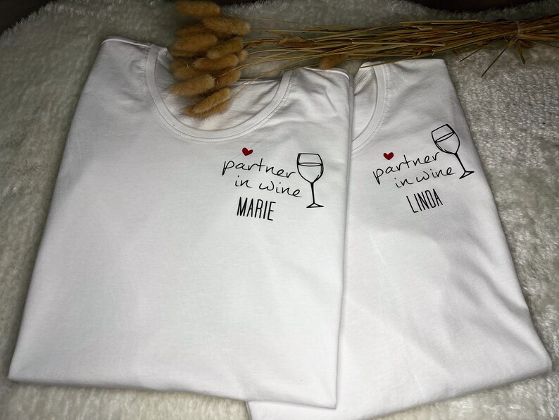 Pu&ograve; includere: Due magliette bianche con il testo "partner in wine" e un'immagine di un bicchiere di vino. Una maglietta dice "Marie" e l'altra dice "Linda".
