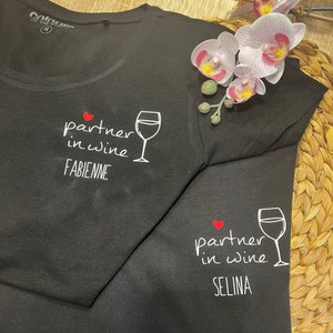 Pu&ograve; includere: Due magliette nere con il testo "partner in wine" e un'immagine di un bicchiere di vino. La prima maglietta ha il nome "FABIENNE" stampato sotto l'immagine. La seconda maglietta ha il nome "SELINA" stampato sotto l'immagine.