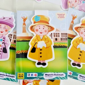May include: A set of three magnetic bookmarks featuring cartoon illustrations of the Queen. Each bookmark has a different colored outfit and a different background. The text "Magnetic Bookmark The Queen" is printed on the bottom of each bookmark.