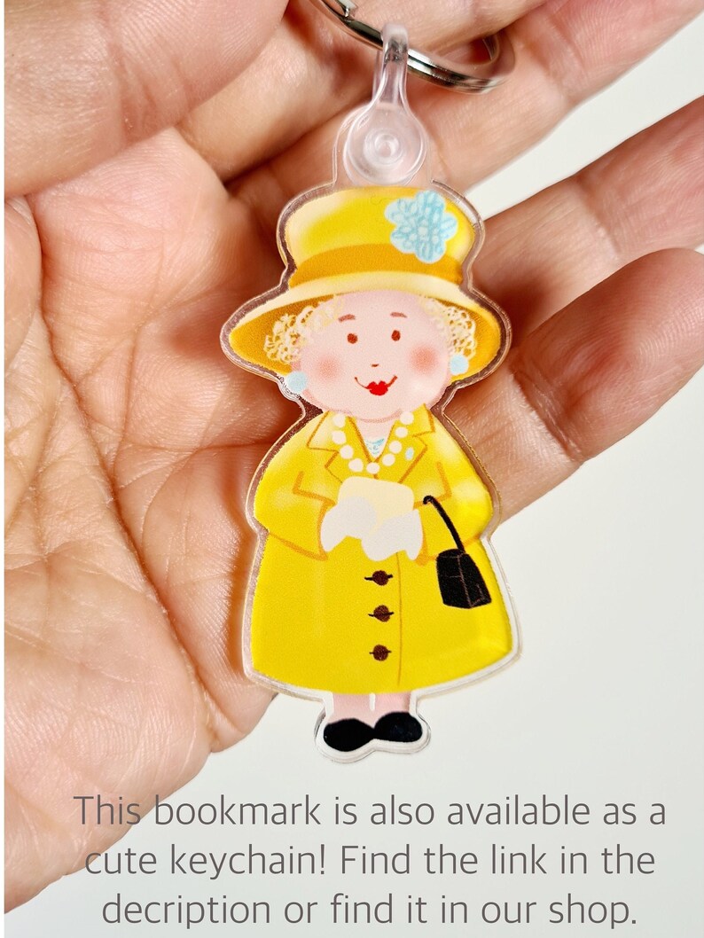 May include: A yellow plastic keychain featuring a cartoon illustration of a woman wearing a yellow dress, a yellow hat with a blue flower, and a black purse. The woman has blonde hair and a smiling face.
