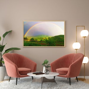 Könnte beinhalten: Zwei rosa Samt-Sessel mit einem weißen Marmor-Couchtisch vor einem gerahmten Druck eines Regenbogens über einem grünen Feld.