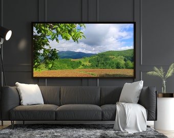 Könnte beinhalten: Ein graues Sofa mit weißen Kissen und einer weißen Wolldecke vor einer schwarzen Wand mit einem gerahmten Landschaftsfoto eines grünen Feldes und Bergen.