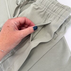 May include: Close-up of a light green pair of pants with a drawstring waist and a pocket on the side.