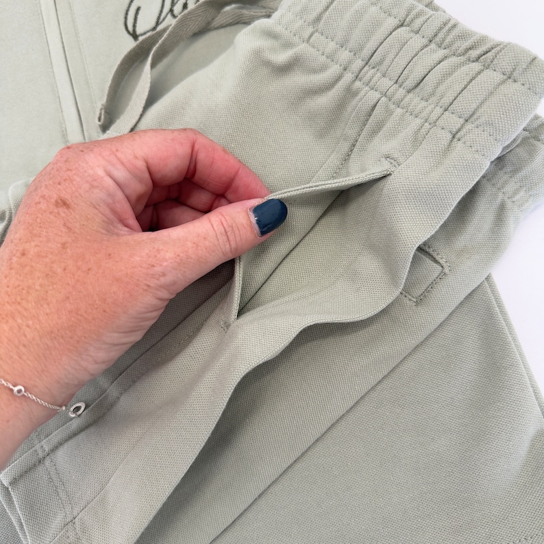 May include: Close-up of a light green pair of pants with a drawstring waist and a pocket on the side.