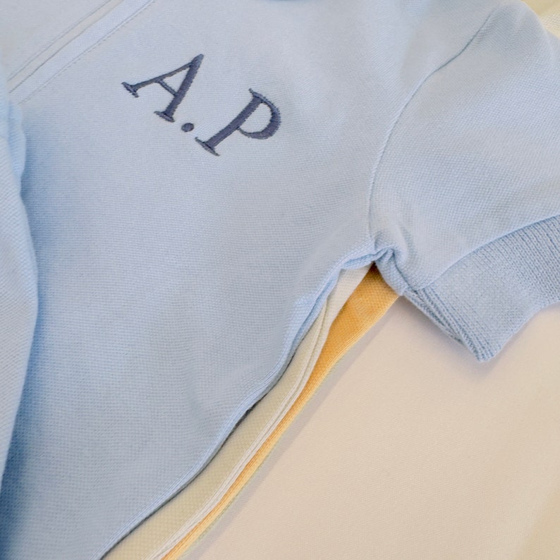 May include: A light blue short-sleeved shirt with a zipper closure and the embroidered initials "A.P."
