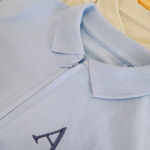 May include: A light blue polo shirt with a zipper closure and a navy blue embroidered letter 'A' on the front.
