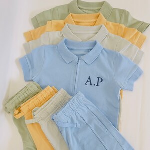 May include: A set of blue, yellow, and green polo shirts and matching pants. The polo shirt has a zipper and the text "A.P." embroidered on the front.
