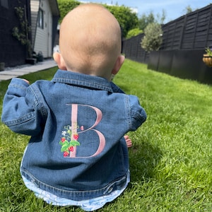 May include: A denim jacket with a pink embroidered letter "B" and strawberry design on the back.