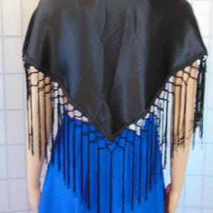 May include: A black satin shawl with fringe trim. The shawl is draped over a person wearing a blue dress.