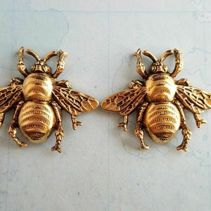 May include: Two gold-toned bee-shaped metal charms with detailed wings and legs.