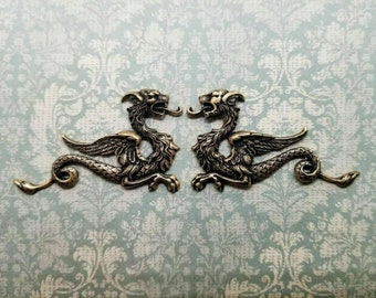Op de afbeelding: Twee gouden metalen drakenfiguren met uitgespreide vleugels en gekrulde staarten. De draken kijken elkaar aan en hebben een gedetailleerd ontwerp.