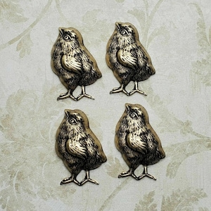 Könnte beinhalten: Vier goldfarbene Metall-Kükenfiguren. Jedes Küken steht aufrecht mit dem Kopf nach oben geneigt und dem Schnabel offen. Die Küken sind mit Federn detailliert und haben ein realistisches Aussehen.