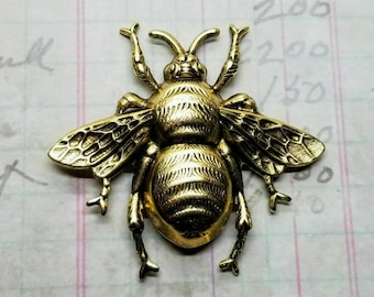 May include: A gold-toned metal bee charm with detailed wings and legs. The bee has a textured body and a realistic design.