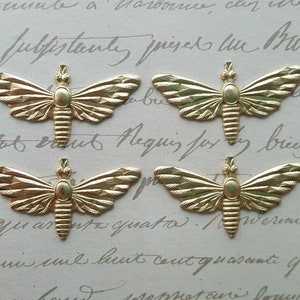 Puede incluir: Cuatro adornos de metal dorado con forma de polilla. Cada polilla tiene alas detalladas y un cuerpo segmentado. Los elementos decorativos están dispuestos sobre un fondo claro con escritura.