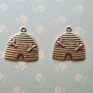 May include: Two gold-toned metal beehive charms with a textured surface and two bees on each charm.