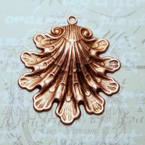 May include: A copper-colored metal pendant shaped like a seashell with a detailed, intricate design. The pendant has a loop at the top for hanging.