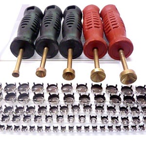 May include: A collection of jewelry tools and components. The image features five tools with black and red handles and brass tips, along with multiple rows of silver-colored bezel settings for jewelry making.