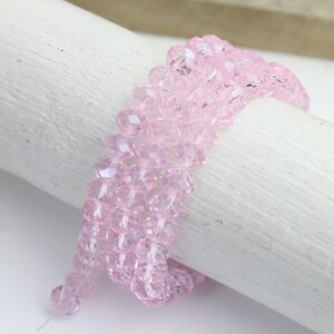 Puede incluir: Una hebra de cuentas de cristal facetadas de color rosa. Las cuentas son pequeñas y tienen un aspecto delicado y brillante.