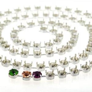May include: A silver-toned metal chain with multiple settings for gemstones, arranged in a spiral pattern. The chain has three gemstones in green, orange, and purple. The background is white.