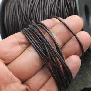 May include: A spool of brown leather cord. The cord is thin and flexible, and it is wound tightly around the spool.