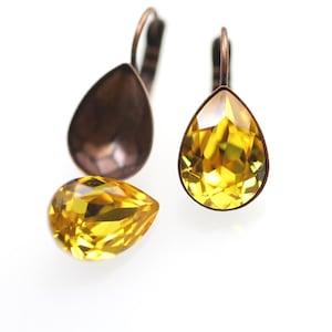 Puede incluir: Un par de pendientes en forma de lágrima con un cristal amarillo y un engaste de metal de tono cobre.