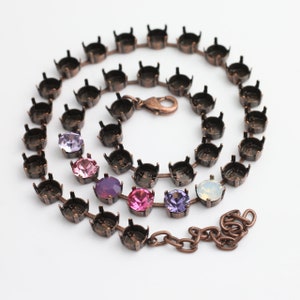 Puede incluir: Un collar con una cadena y cierre de color cobre. La cadena presenta engastes vacíos y varias piedras preciosas de colores en tonos rosas, morados e iridiscentes. El collar se muestra sobre un fondo blanco.
