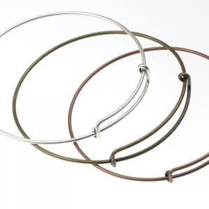 Op de afbeelding: Drie armbandjes in verschillende metaalafwerkingen: zilver, brons en koper. De armbandjes zijn allemaal open en hebben een eenvoudig, elegant ontwerp.