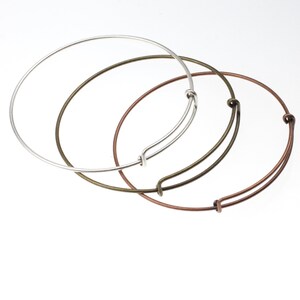 May include: Three bangle bracelets in different metal finishes: silver, bronze, and copper. The bracelets are all open and have a spring clasp.